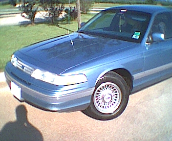 1994 Ford Crown Victoria - A blue sedan is parked on a paved surface with grass and trees in the background.