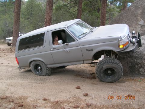 1985 Ford Bronco - A gray Ford Bronco navigates rough terrain, with another white vehicle visible in the background.