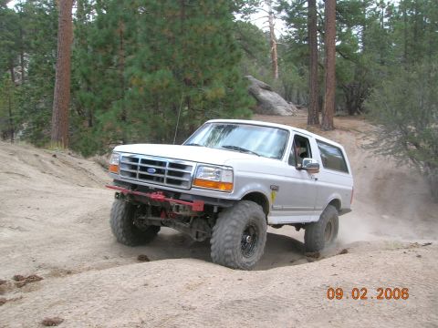 1985 Ford Bronco - A white 1992 Ford Bronco navigates a dusty off-road path surrounded by trees.
