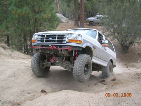 1985 Ford Bronco - A modified Ford Bronco navigates a dusty off-road path with another vehicle visible in the background.