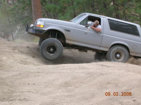 1985 Ford Bronco - Silver Ford Bronco navigates a sandy incline, kicking up dust.