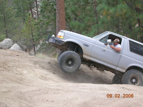 1985 Ford Bronco - A man drives a lifted Ford Bronco off-road on a sunny day.