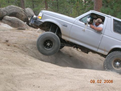 1985 Ford Bronco - A silver Ford Bronco navigates a steep dirt incline, its front tire lifted off the ground.