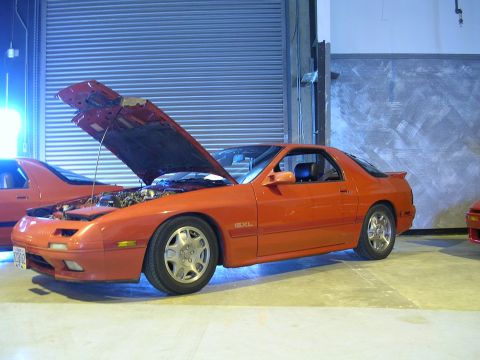 1996 Ford Probe - Orange Mazda RX-7 with hood open, parked indoors next to another vehicle.