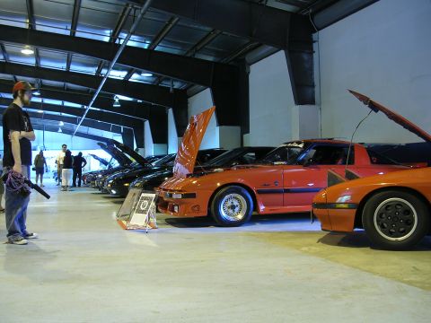 1996 Ford Probe - A row of cars, mostly orange, are displayed indoors with their hoods up, and a person stands nearby with a leaf blower.