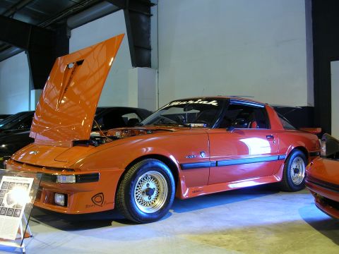 1996 Ford Probe - An orange Mazda RX-7 is displayed with its hood open, revealing the engine bay.