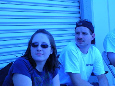1996 Ford Probe - Two individuals are seated outdoors, with a blue corrugated metal wall serving as the backdrop. The man is wearing a white t-shirt with vis…