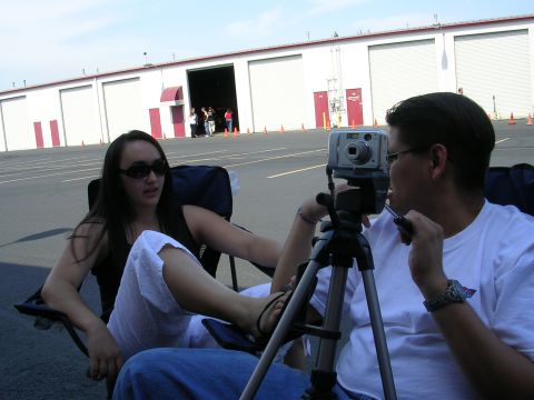 1996 Ford Probe - Two people are seated in chairs, one operating a camera on a tripod, with a row of garage doors in the background.