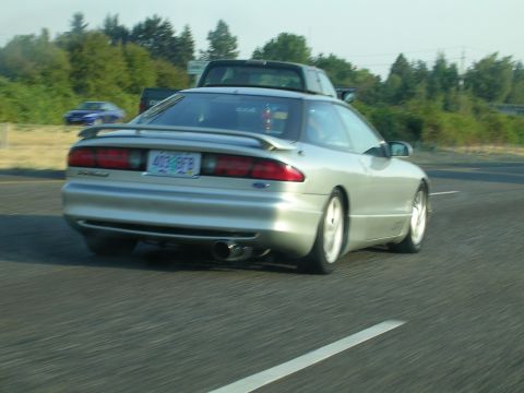 1996 Ford Probe - A silver coupe drives on the highway, with a pickup truck behind it.