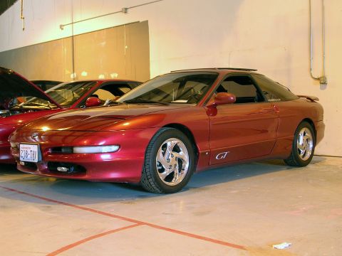 1996 Ford Probe - A red 1996 Ford Probe GT coupe is parked indoors next to another red vehicle.