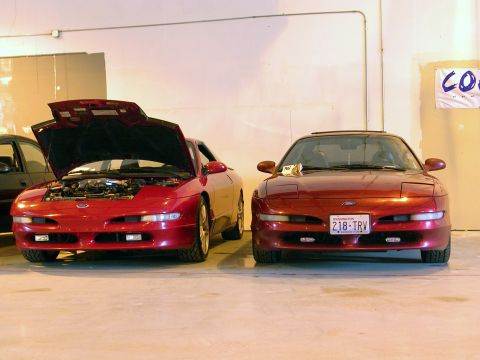 1996 Ford Probe - Two red Ford Probes are displayed indoors, with one vehicle's hood open to reveal the engine compartment.