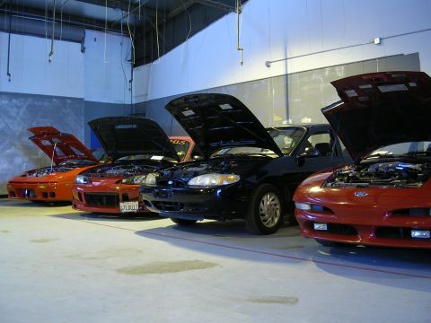 1996 Ford Probe - A row of cars, each with its hood raised, are parked indoors on a concrete floor.