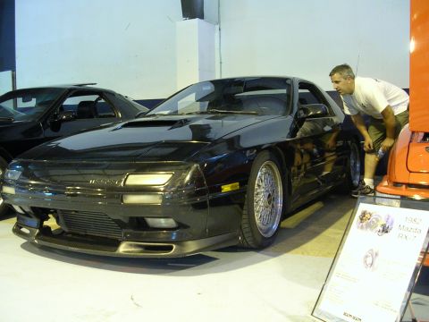 1996 Ford Probe - A black Mazda RX-7 is displayed indoors next to another vehicle, with a sign indicating it is a 1982 model.