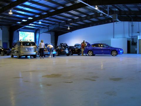 1996 Ford Probe - People are gathered around several vehicles inside a spacious, well-lit warehouse.