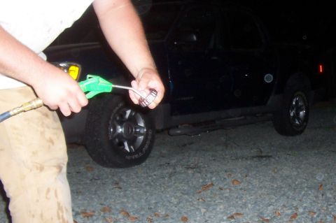 1994 Ford F-150 - A person uses an air gun to clean a metal bearing near the wheel of a dark SUV.