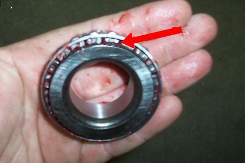 1994 Ford F-150 - A wheel bearing, possibly from a 1994 Ford F-150, is held in a hand with a red arrow indicating the rollers.