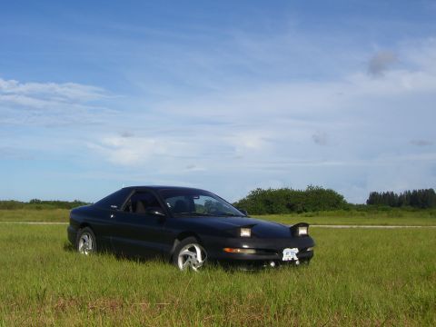 1994 Ford Probe - A black coupe with pop-up headlights sits in a grassy field on a partly cloudy day.