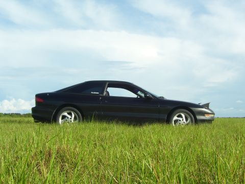 1994 Ford Probe - A black 1994 Ford Probe is seen from the side in a grassy field with a blue sky overhead.