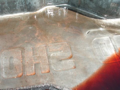 1993 Ford Taurus - Metal part with embossed text and reddish fluid, possibly from an engine or transmission.