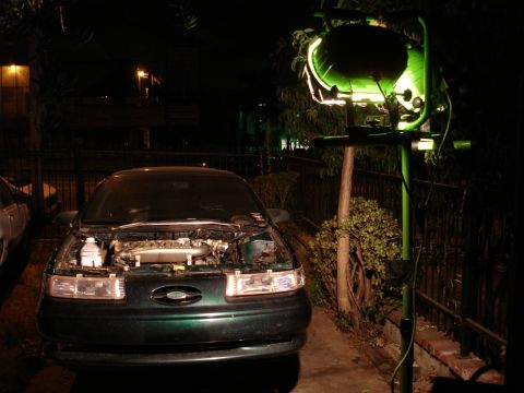 1993 Ford Taurus - A green sedan sits in a driveway at night with its hood open, illuminated by a large work light.