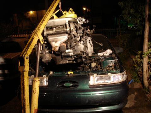 1993 Ford Taurus - Engine hoist lifting an engine from a dark green Ford Taurus.