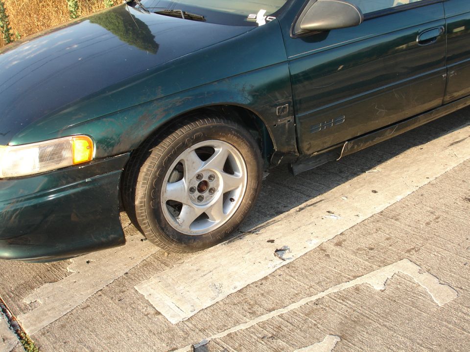 Dirty dark green Ford Taurus SHO front wheel and fender with five-spoke alloy