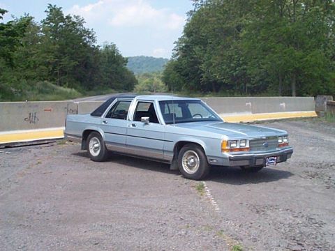 1991 Ford Crown Victoria - Light blue 1991 Ford Crown Victoria sedan parked on a gravel road with trees in the background.