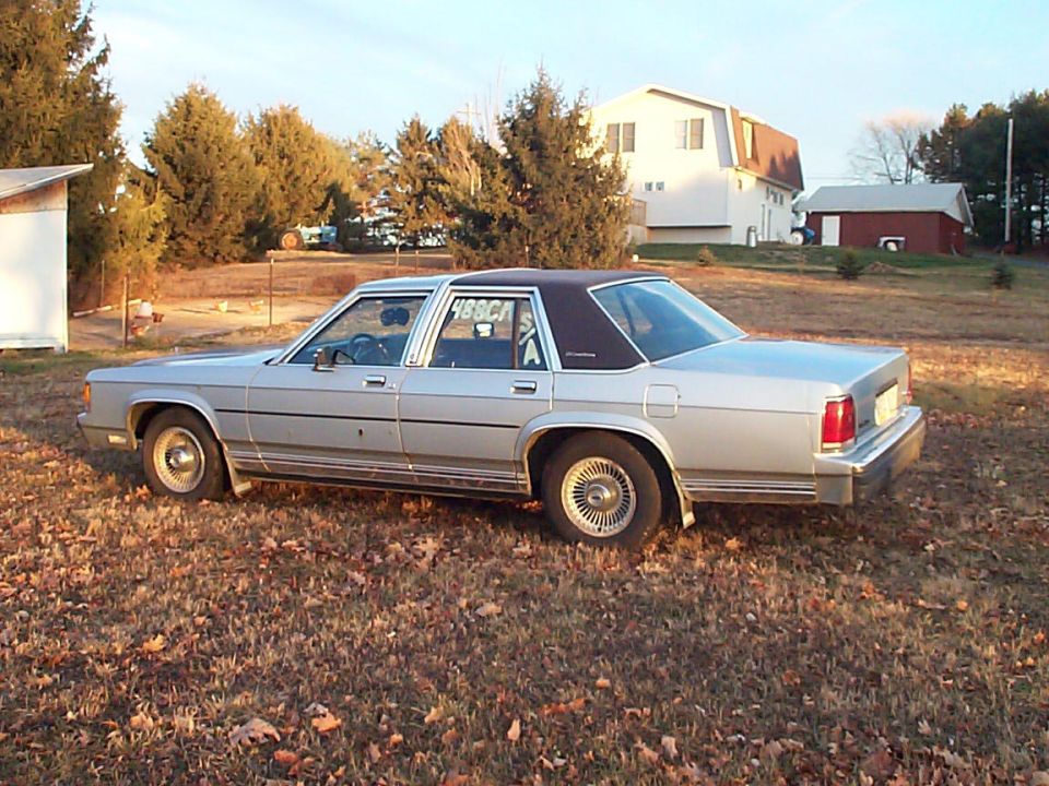 Silver-blue Ford Crown Victoria sedan with blue vinyl top and wire wheel covers on autumn lawn