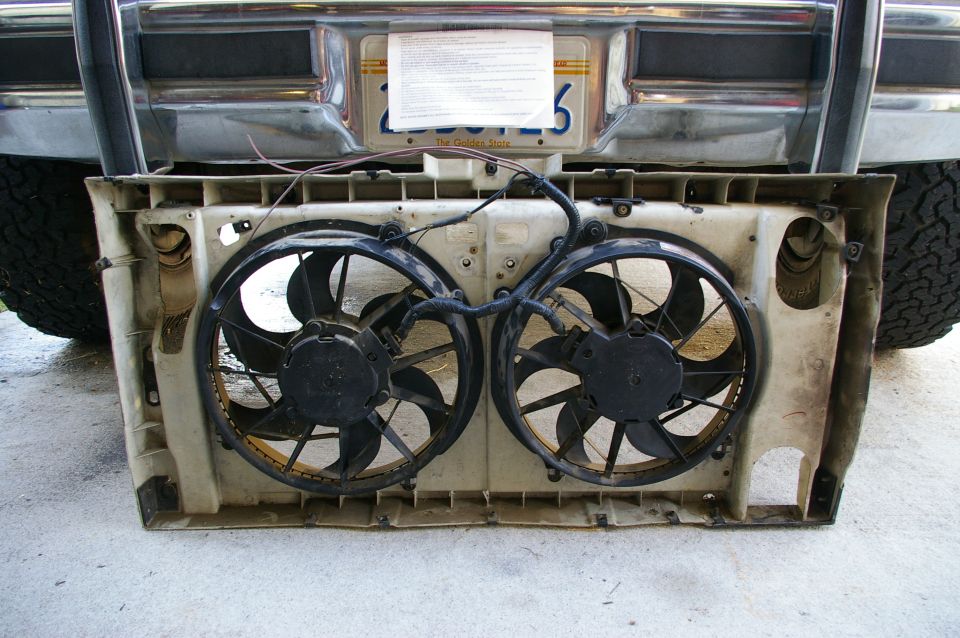 dual electric fans mounted in a plastic shroud, with part of a truck bumper and tire visible behind