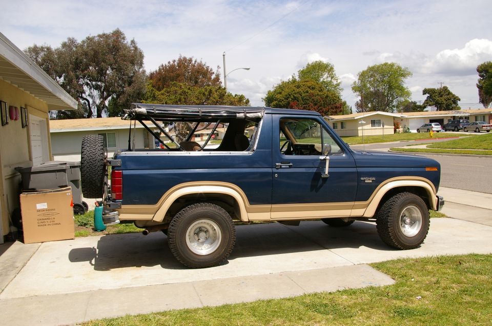 Blue and tan Ford Bronco with a soft top frame, parked on a driveway