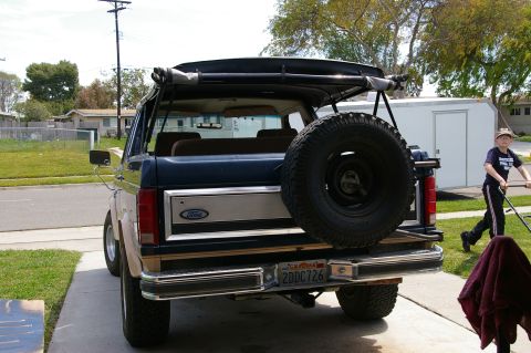 1986 Ford Bronco - Rear view of a Ford Bronco with a soft top, showing its spare tire and California license plate.