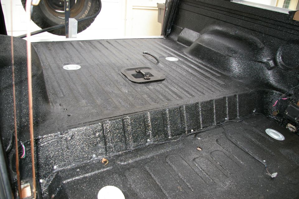 Cargo bed sprayed with textured black bedliner over ribbed floor and wheel well