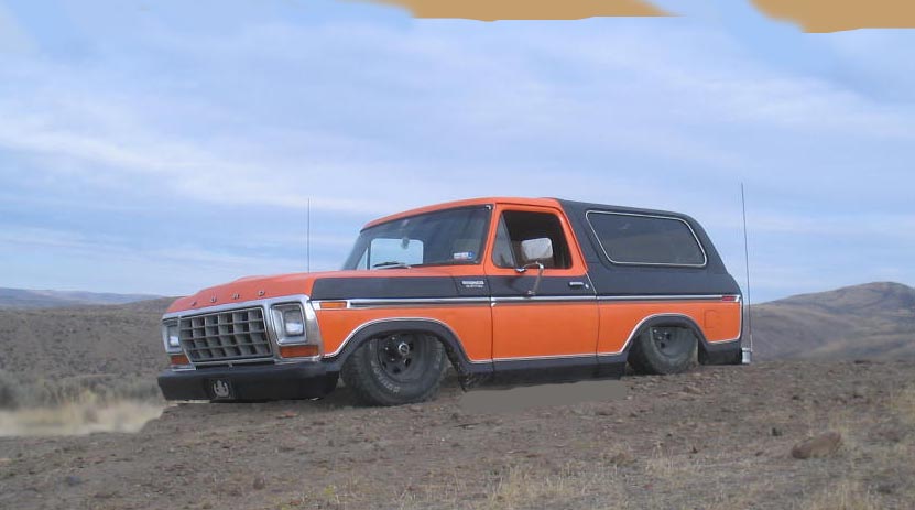 Orange and black Ford Bronco lowered on black wheels, parked on a dirt hill