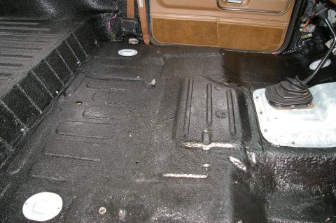 1986 Ford Bronco - Bare interior floor of a stripped SUV sprayed in textured black bedliner, with the ribbed cargo floor, seat-belt bolt holes and metal-rimme…