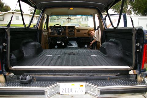 1986 Ford Bronco - Rear view into a gutted full-size SUV with the tailgate down and rear glass up, showing the entire cargo floor and wheel tubs sprayed in te…
