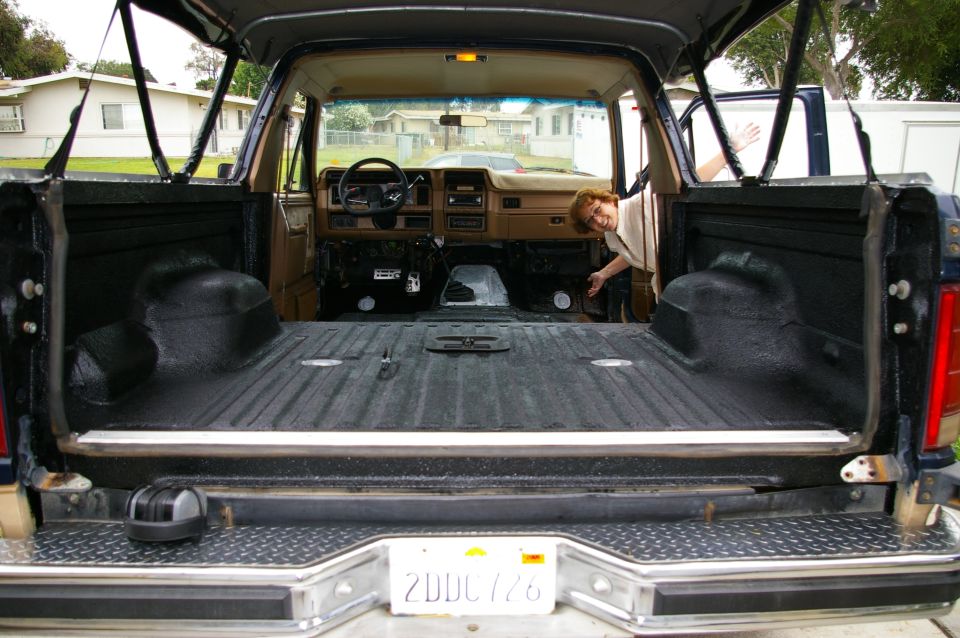 Rear view into bedliner-coated cargo area of a gutted SUV with tailgate down and tan interior