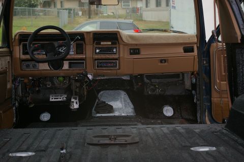 1986 Ford Bronco - Stripped interior of a blue SUV shot from the cargo floor toward the tan dash, with both seats removed and the entire floor sprayed in blac…