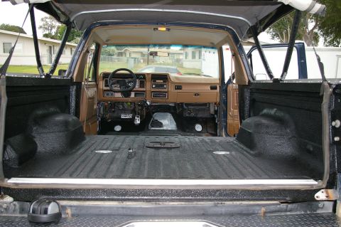 1986 Ford Bronco - View through the dropped tailgate of a blue full-size SUV with the seats removed, showing the whole rear tub and wheel wells coated in text…