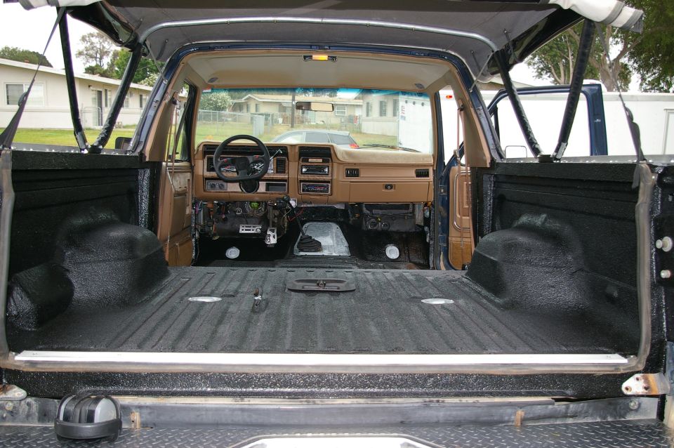 Bedliner-coated rear tub of blue SUV seen through open tailgate, tan dash beyond