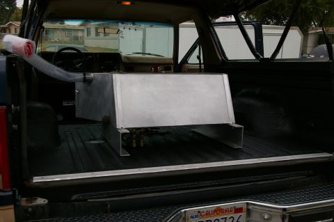 1986 Ford Bronco - Rear view into a stripped SUV cargo area coated in black bedliner, with a large fabricated aluminum fuel cell mounted on welded aluminum cr…