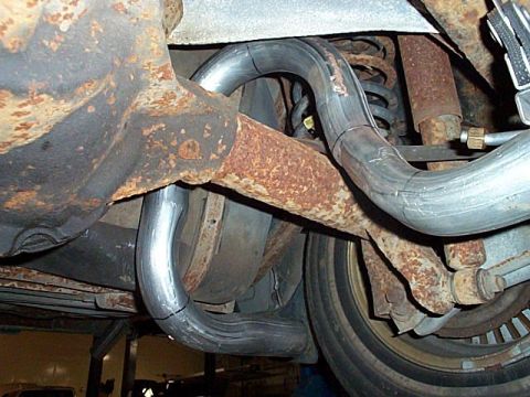 1991 Ford LTD Crown Victoria - Underbody shot of a car on a lift showing a pair of new dual exhaust pipes bent up and over the rear axle housing, the fresh aluminized tub…
