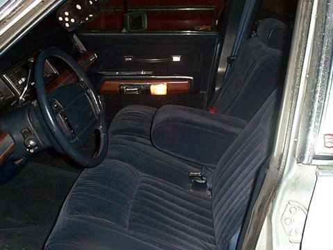 1991 Ford LTD Crown Victoria - Interior of a full-size sedan shot through the open driver's door, showing dark blue cloth split bench seats with a fold-down center armres…