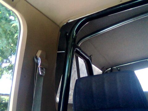 1989 Ford Bronco - The interior of a vehicle shows a roll cage structure and a dark-colored seat with a seatbelt.