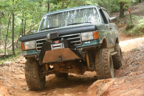 1990 Ford Bronco - 1990 Ford Bronco navigating an off-road trail with large tires and a winch installed.