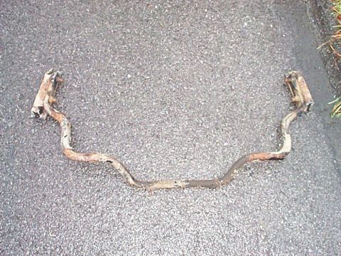 1991 Ford LTD Crown Victoria - A removed rear anti-roll (sway) bar lying on asphalt pavement, its tubular steel body bent in the typical U-shape with formed offsets and f…