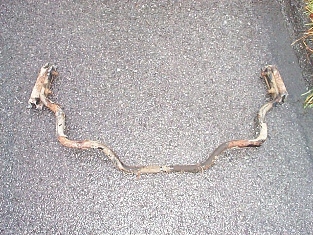 Rusty removed rear sway bar lying on asphalt pavement
