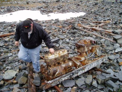 2000 Ford E350 - Man inspects a heavily rusted engine block mounted on a metal frame in a rocky, outdoor environment.