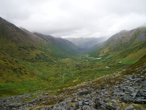 2000 Ford E350 - A vast mountain valley with a winding stream and green slopes under a heavy overcast sky.