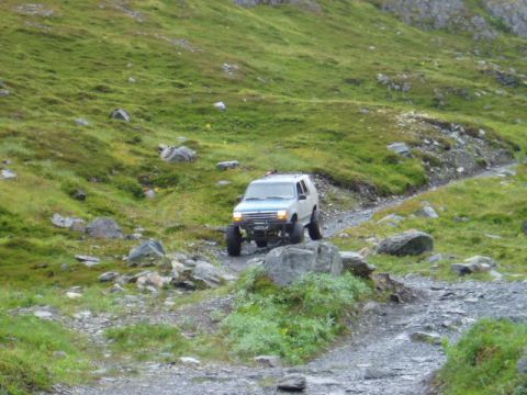2000 Ford E350 - A white 1997 Ford Explorer navigates a , rocky trail in a mountainous, grassy landscape.