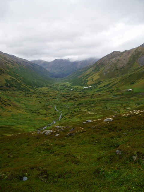 2000 Ford E350 - A vast mountain valley landscape under a cloudy sky, with a stream flowing through the green terrain.